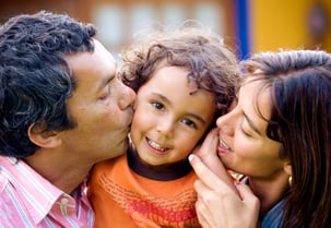 parents kissing son portrait outdoors at home - kid is smiling